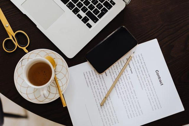 Contract document on a table beside a laptop, smartphone, and pencil.