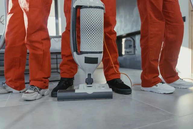 Three janitorial personnel standing together while holding their cleaning equipment.