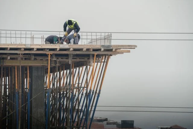 Three construction workers performing building work on scaffolding at a construction site.
